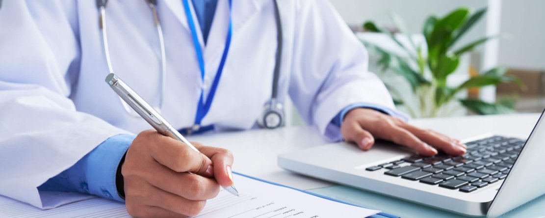 Doctor checking information in computer program before filling medical card